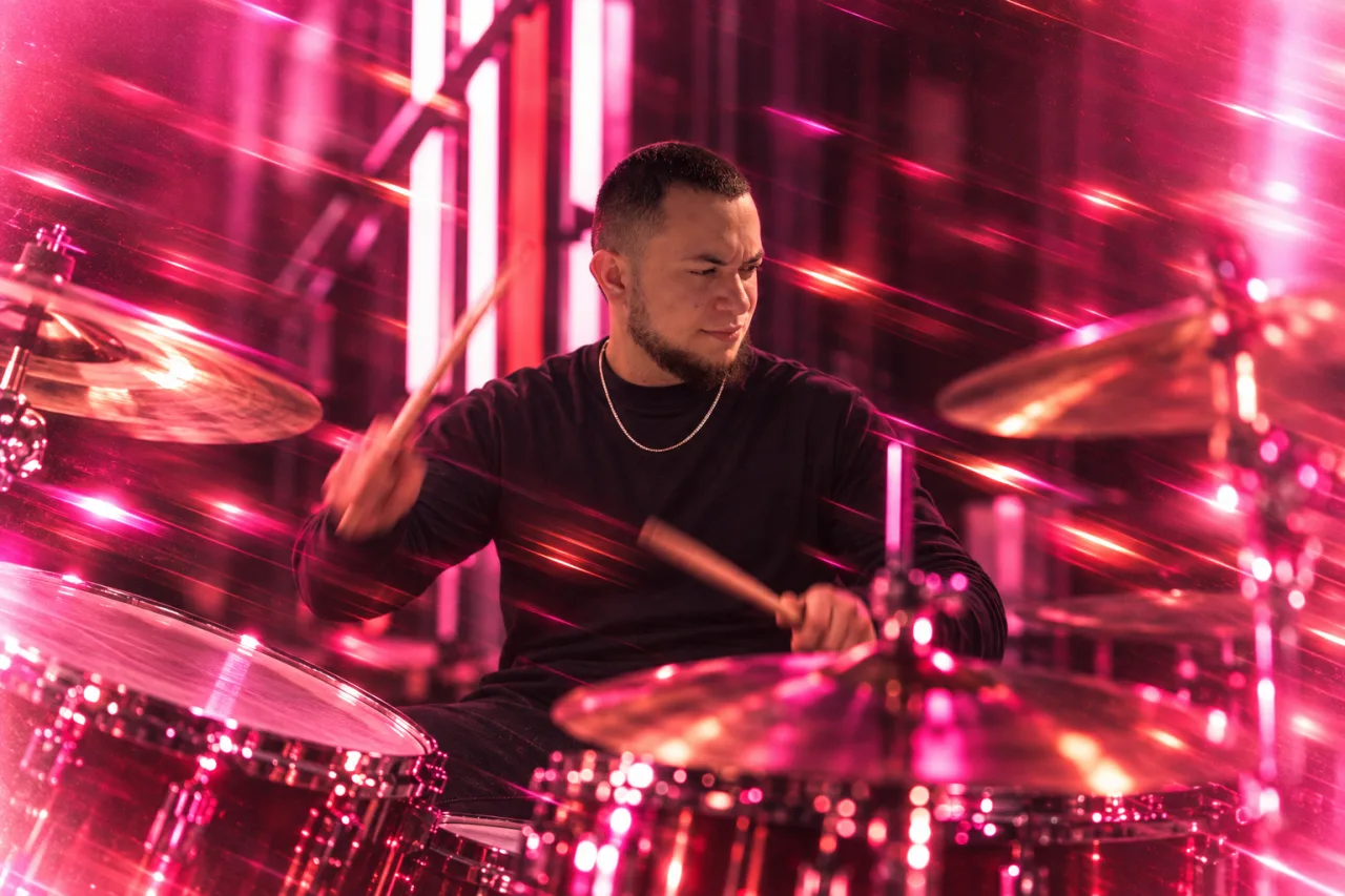 Matheus tocando bateria, com luzes rosa e rastros de movimento